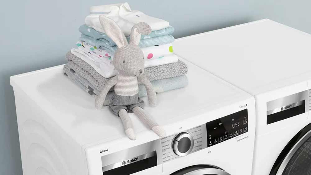 Set spotřebičů Bosch, kdy na jednom z nich je nahoře poskládaná kupička dětského oblečení a háčkovaný zajíček_05