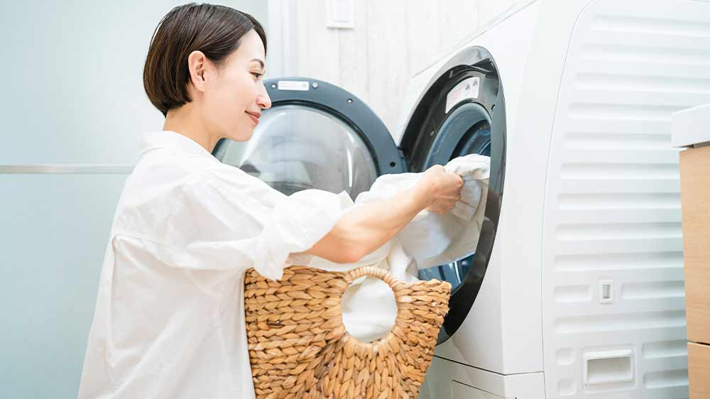 Asijská žena vyndává bílé prádlo z pračky do proutěného košíku na klíně_03