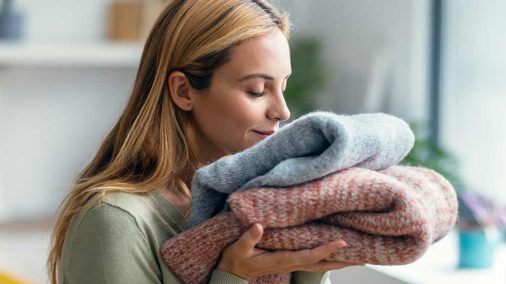 Žena si s úsměvem čichá k vypraným svetrům_03