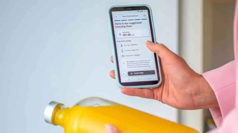 Ženské ruce držící mobilní telefon se zapnutou aplikací hOn v pravé ruce a v levé pak lahev s džusem_04