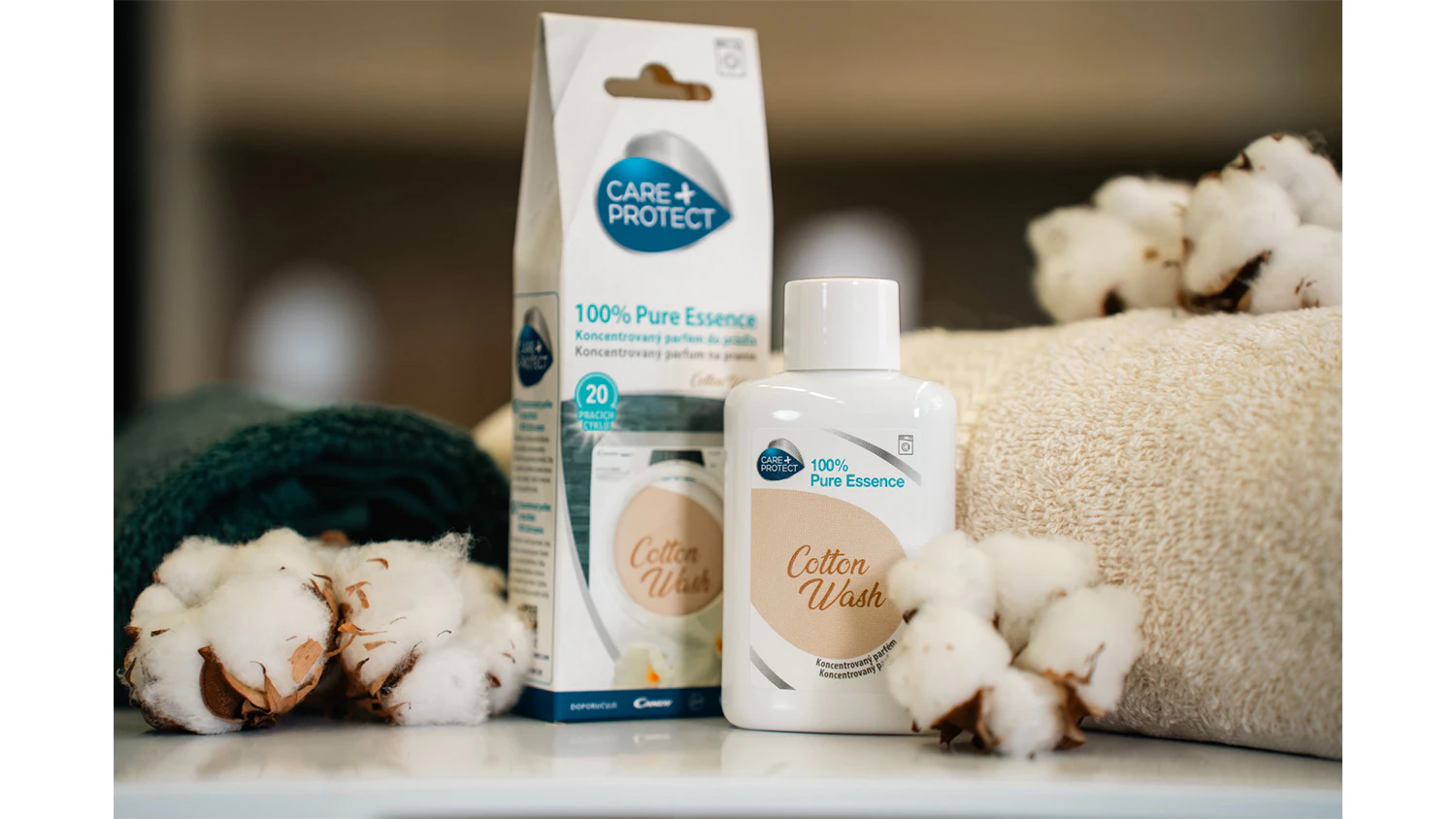 Vůně do su&scaron;ičky Cotton Wash stoj&iacute; vedle balen&iacute; mezi ručn&iacute;ky a bavlnou