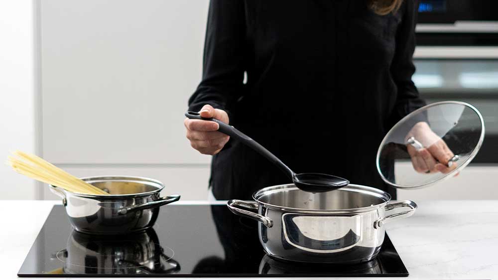 Žena vaří jídlo v hrncích na sklokeramické varné desce_02