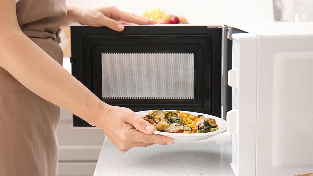 Žena dává talíř s jídlem do mikrovlnné trouby_02