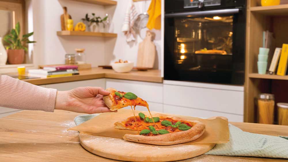 Ženská ruka si bere dílek skvěle vypadající pizzy upečené v troubě elektrického sporáku GORENJE G600 GEC5C42WG_02
