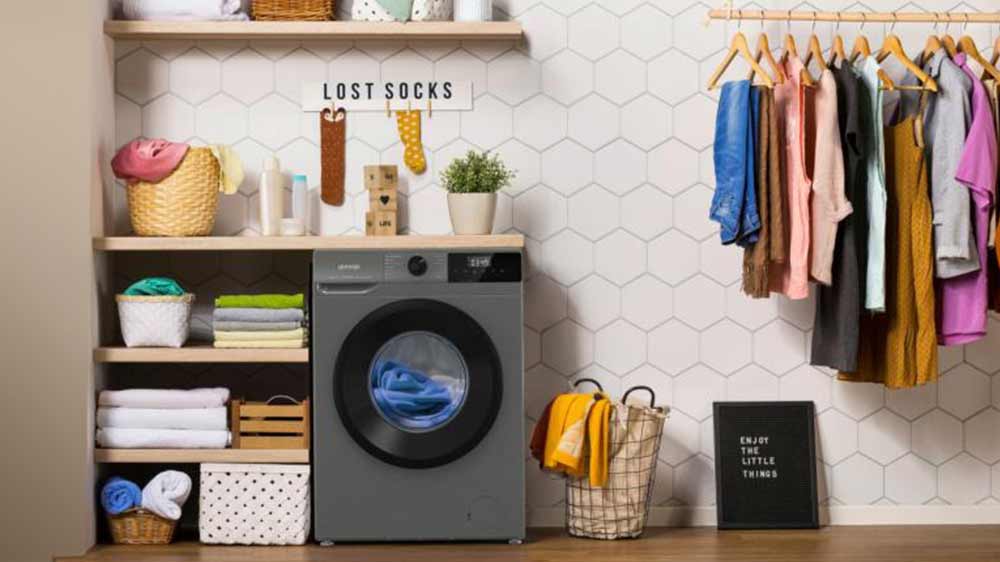 Automatická pračka Gorenje WNHPI84AS/A stojící v prostoru šatny vedle polic s ručníky a stojanem na oblečení_02