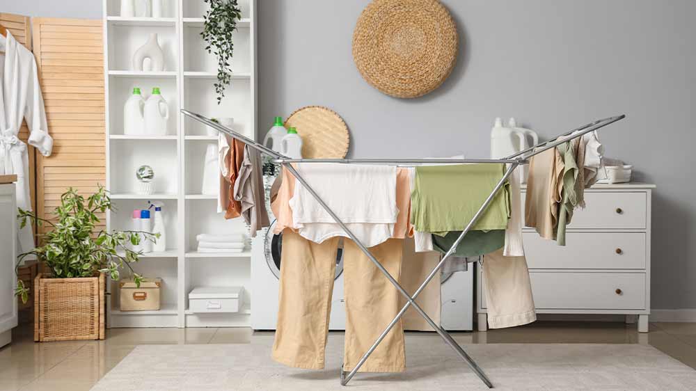 Prádlo na sušáku uprostřed prádelny a v pozadí stojící bílá pračka a sušička_03