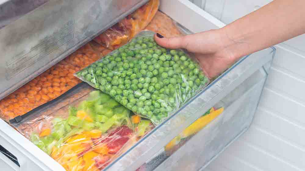 Ženská ruka vytahuje z mrazáku sáček s hráškem_02