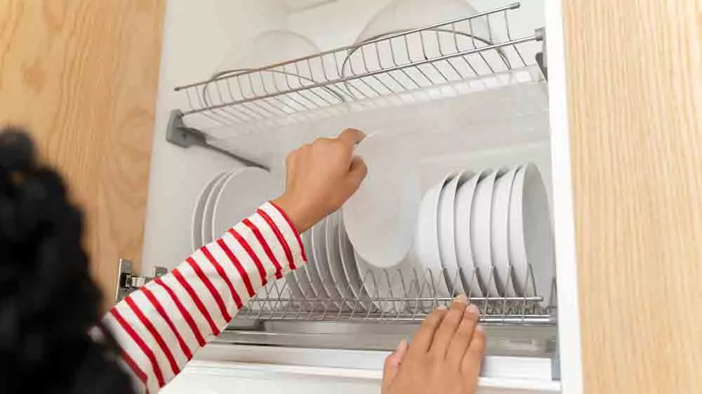 Žena vkládá čisté talíře do skříňky