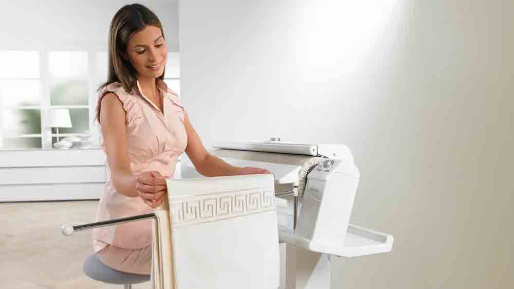 Žena d&aacute;v&aacute; vyžehlen&eacute; pr&aacute;dlo na odkl&aacute;dac&iacute; tyč mandlu Miele B 995 D_05