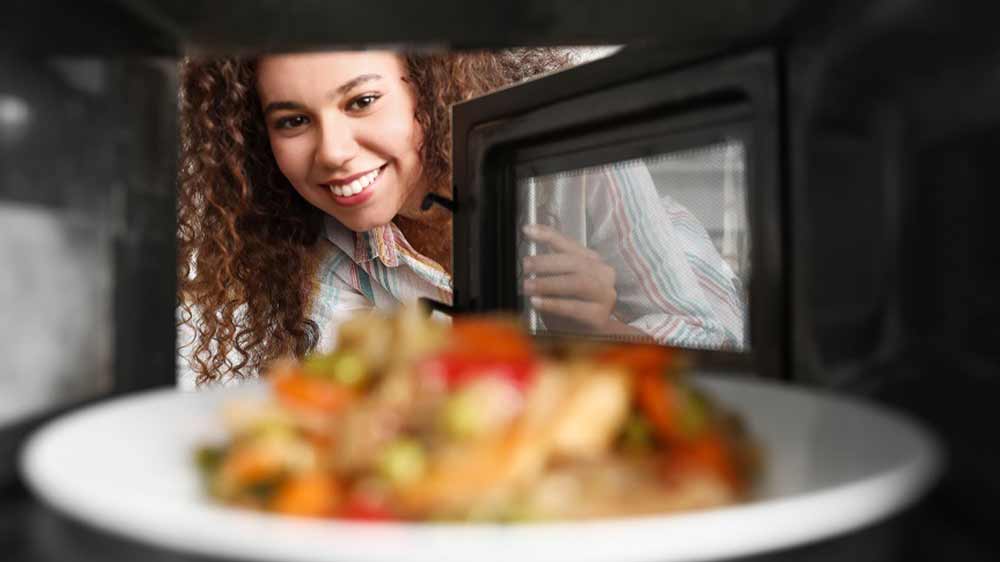 Pohled z prostoru mikrovlnn&eacute; trouby s tal&iacute;řem j&iacute;dla na ženu otev&iacute;raj&iacute;c&iacute; dv&iacute;řka trouby_03