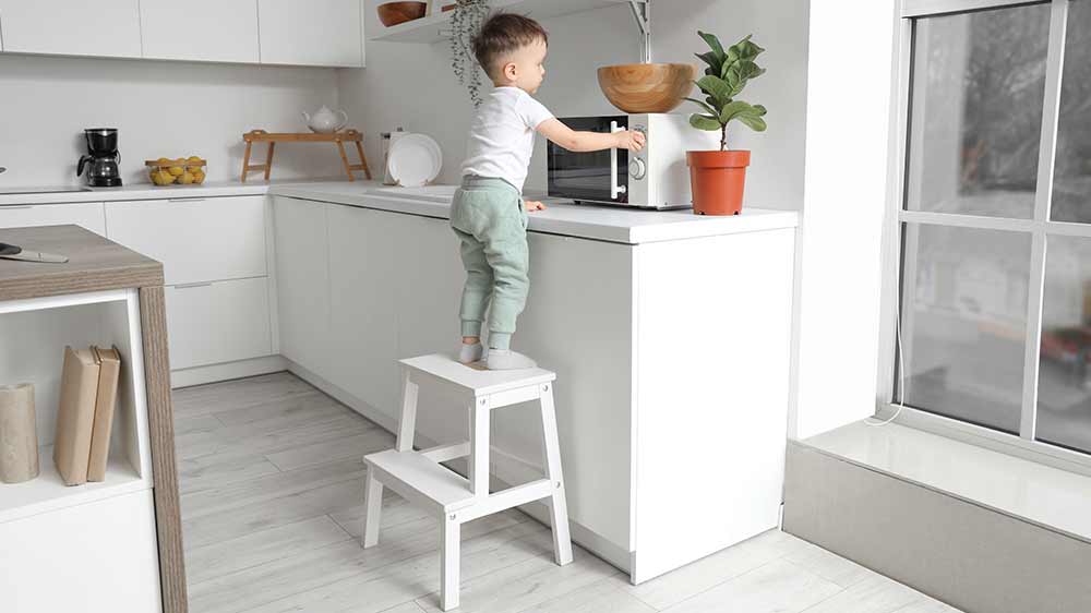 Mal&yacute; chlapec stoj&iacute;c&iacute; na schůdc&iacute;ch u kuchyňsk&eacute; linky a manipuluj&iacute;c&iacute; s mikrovlnnou troubou_05