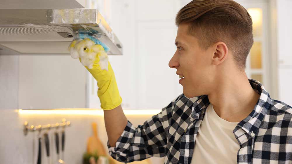 Mladý muž, který umývá komínovou digestoř napěněnou houbičkou na nádobí_05