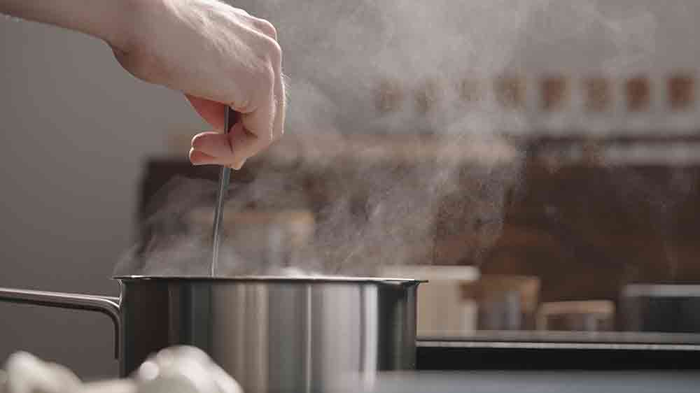 Mužská ruka míchá jídlo v hrnci, ze kterého stoupá pára_03