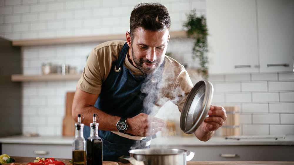 Muž nakl&aacute;něj&iacute;c&iacute; se nad hrnec a nadzved&aacute;vaj&iacute;c&iacute; pokličku_03