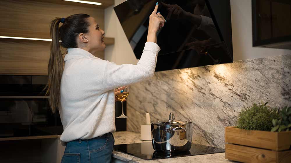 Mlad&aacute; žena ovl&aacute;daj&iacute;c&iacute; kom&iacute;novou digestoř v kuchyni_04