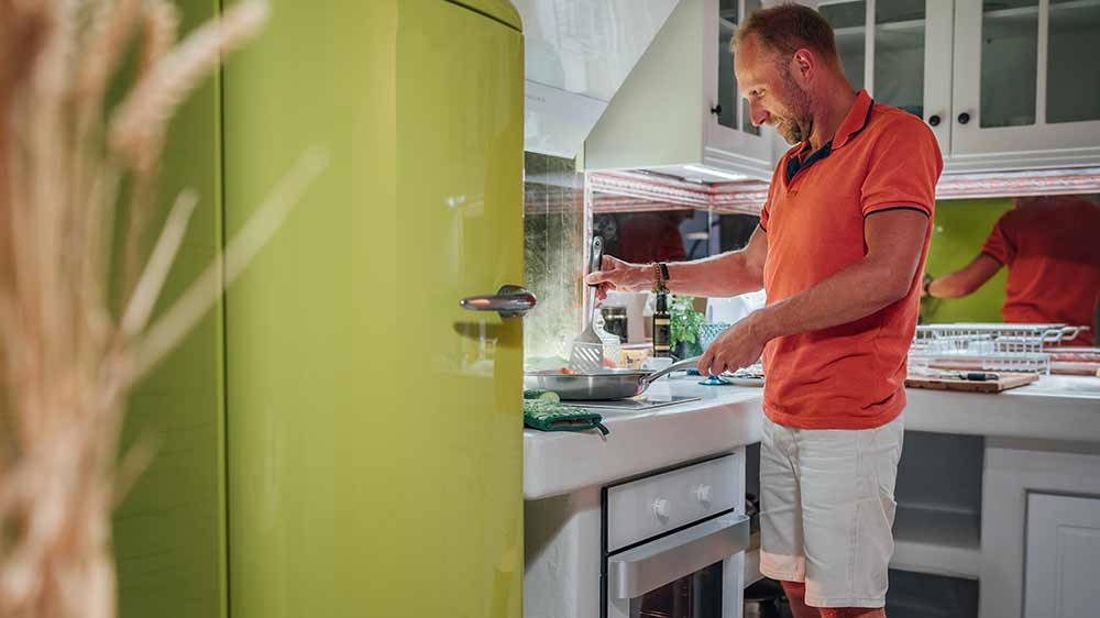 Muž připravuj&iacute;c&iacute; j&iacute;dlo na spor&aacute;ku a nad n&iacute;m b&iacute;l&aacute; kom&iacute;nov&aacute; digestoř_05