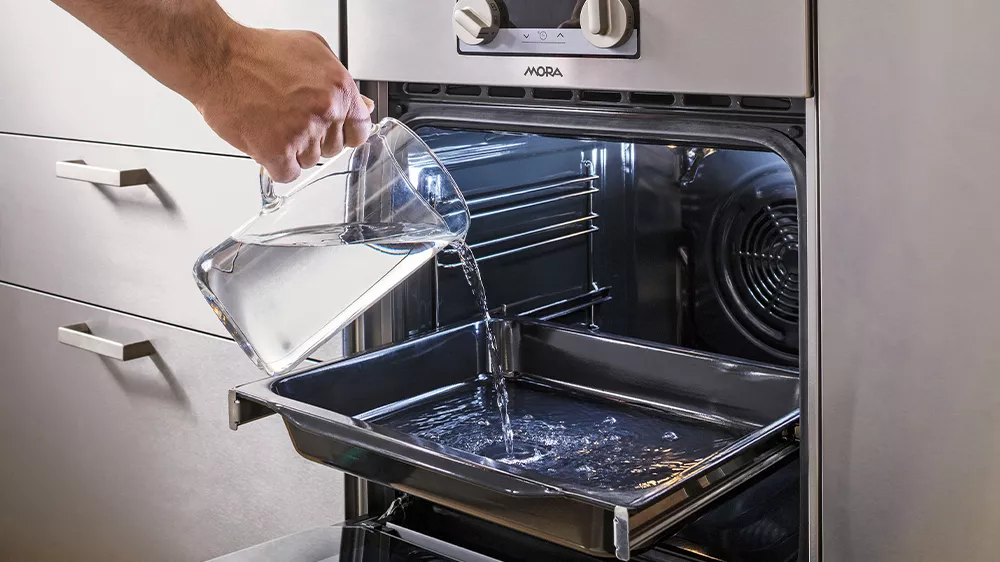 Muž lij&iacute;c&iacute; vodu na plech k EcoClean hydrolytick&eacute;mu či&scaron;těn&iacute; kombinovan&eacute;ho spor&aacute;ku MORA K 5655BW_05