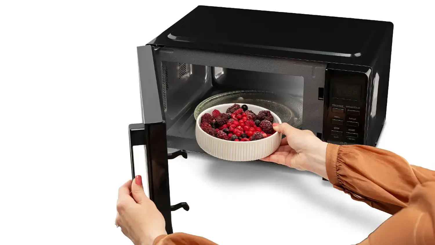 Žensk&aacute; ruka vkl&aacute;d&aacute; misku s mražen&yacute;m ovocem do mikrovlnn&eacute; trouby MORA