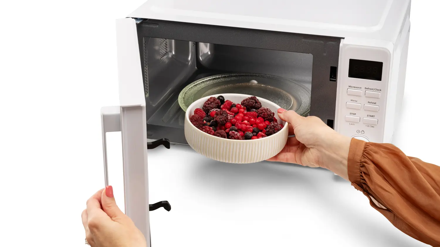 Žensk&aacute; ruka vkl&aacute;d&aacute; misku s mražen&yacute;m ovocem do mikrovlnn&eacute; trouby MORA