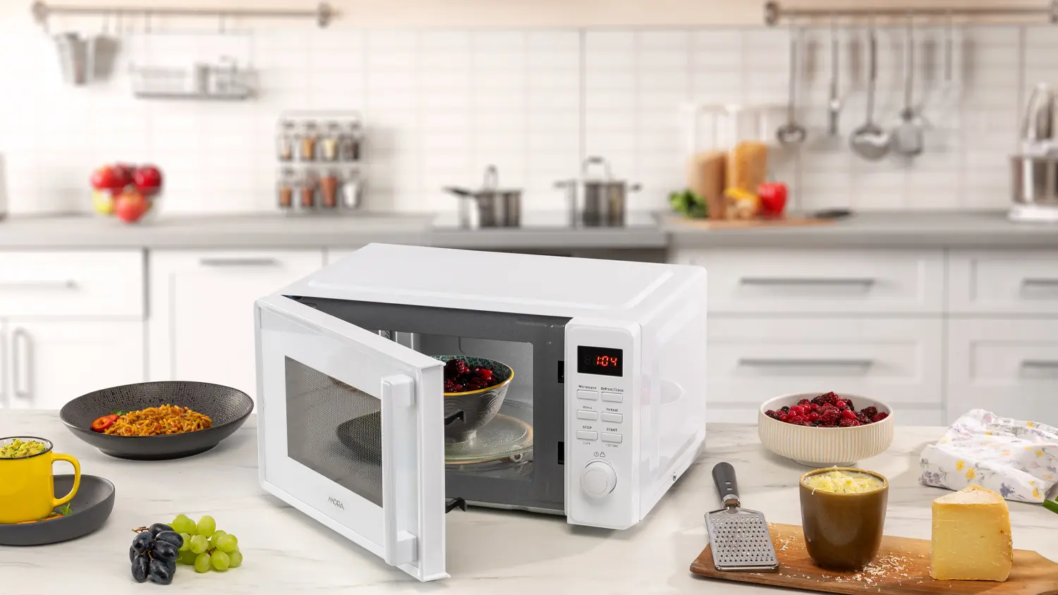 Miska s rozmrazen&yacute;m ovocem v mikrovlnn&eacute; troubě MORA a hotov&yacute; popcorn a dal&scaron;&iacute; j&iacute;dlo stoj&iacute;c&iacute; vedle na kuchyňsk&eacute; lince