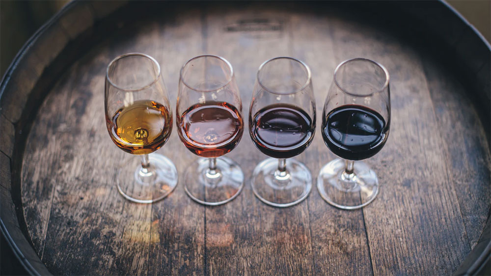 Čtyři čiré sklenky s různými druhy vína na dubovém sudu