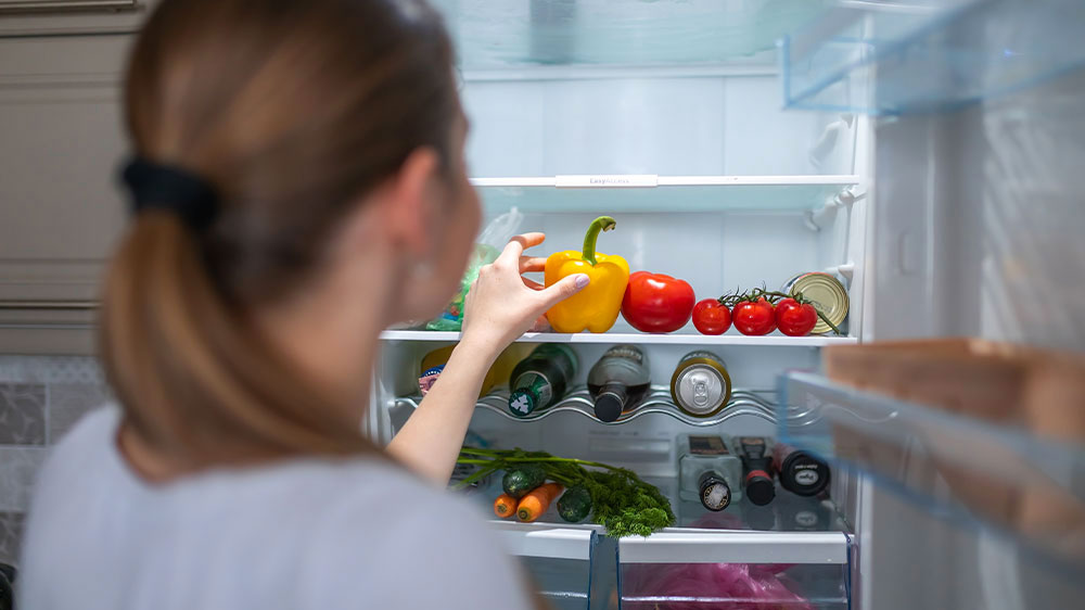 Dívka stojí u otevřené lednice a sahá po paprice_03