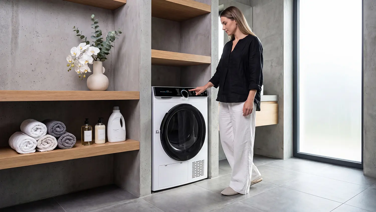 Žena stojí u ovládacího panelu sušičky Philco PDCI 9 C King 3 v moderní koupelně.