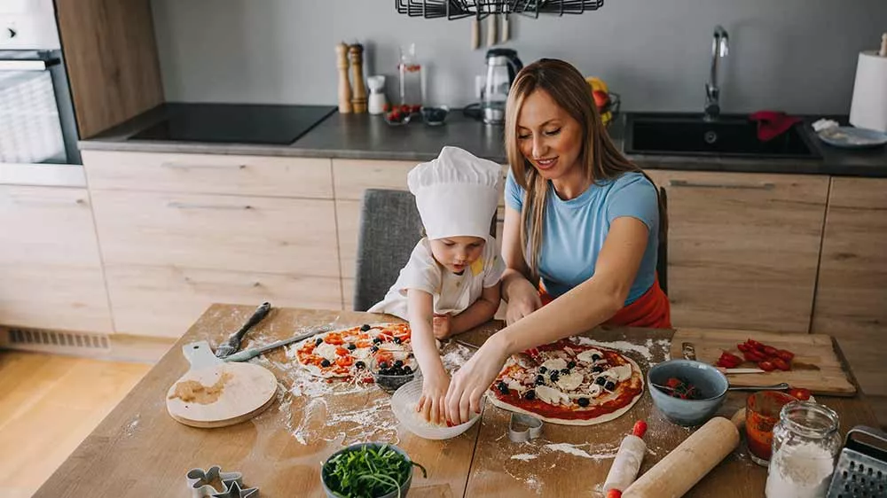 Matka s dcerou v kuchařské čepici připravují pizzu u kuchyňského ostrůvku_04