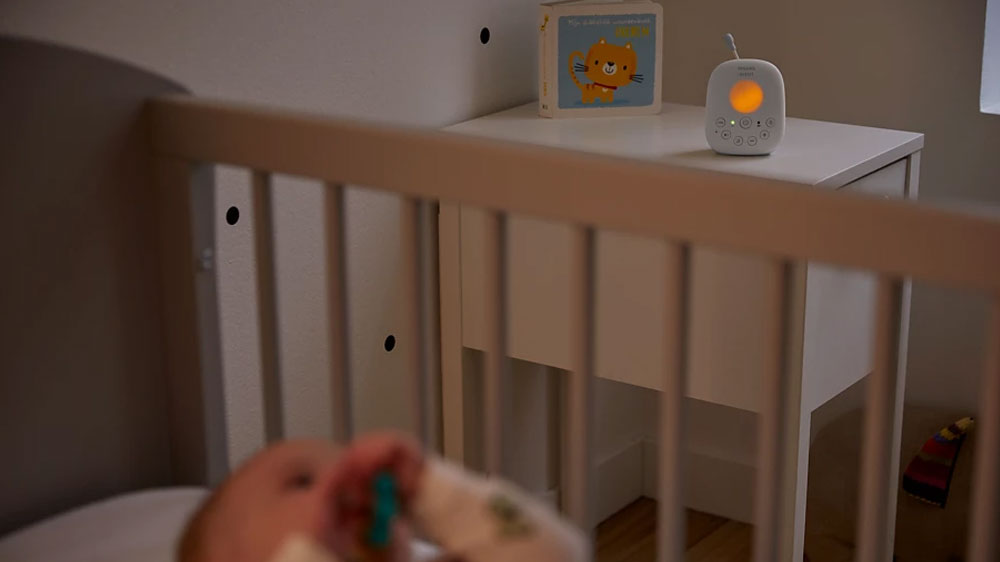 Miminko ležící v postýlce a na nočním stolku položená audio dětská chůvička Philips Avent Advanced SCD 715/52 se zapnutým nočním světlem_04