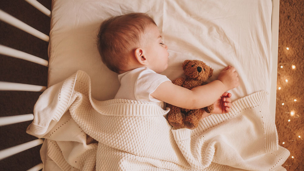 Batole spící pod dekou v postýlce objímající plyšového medvídka_04