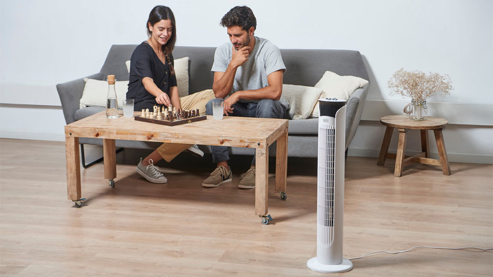 Muž se ženou hraj&iacute; &scaron;achy v ob&yacute;vac&iacute;m pokoji vedle sloupov&eacute;ho ventil&aacute;toru Black+Decker BXEFT48E_02