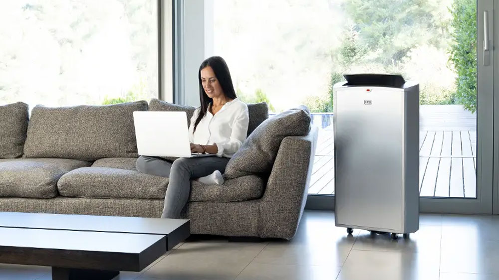 Žena sedí na pohovce vedle mobilní klimatizace BLACK+DECKER BXAC12000E_02