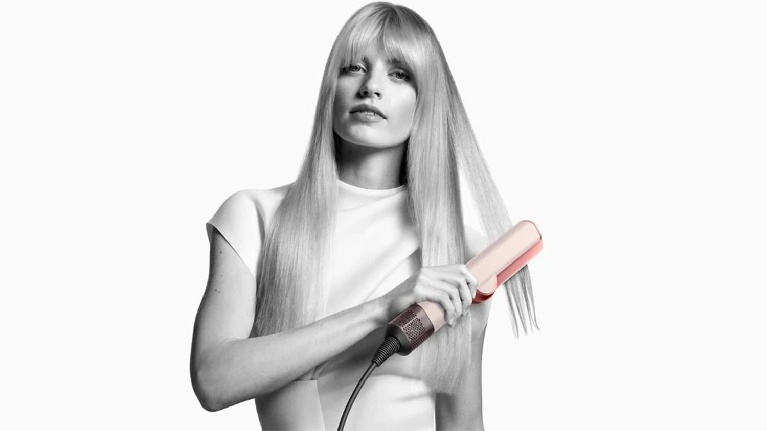 Žena si upravuje vlasy žehličkou Dyson