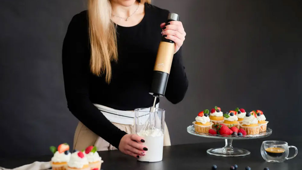 Žena šlehající šlehačku v nádobě tyčovým mixérem ETA Mano 3219 90020 na pracovní desce mezi podnosy s mufiny_02