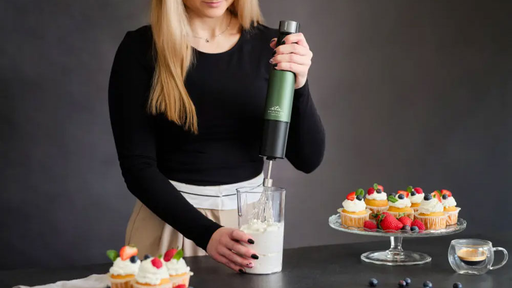 Žena šlehající šlehačku v nádobě tyčovým mixérem ETA Mano 3219 90030 na pracovní desce mezi podnosy s mufiny_02