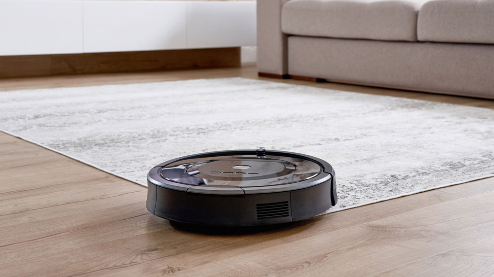 Robotický vysavač přejíždějící z tvrdé podlahy na koberec v obývacím pokoji před pohovkou_05