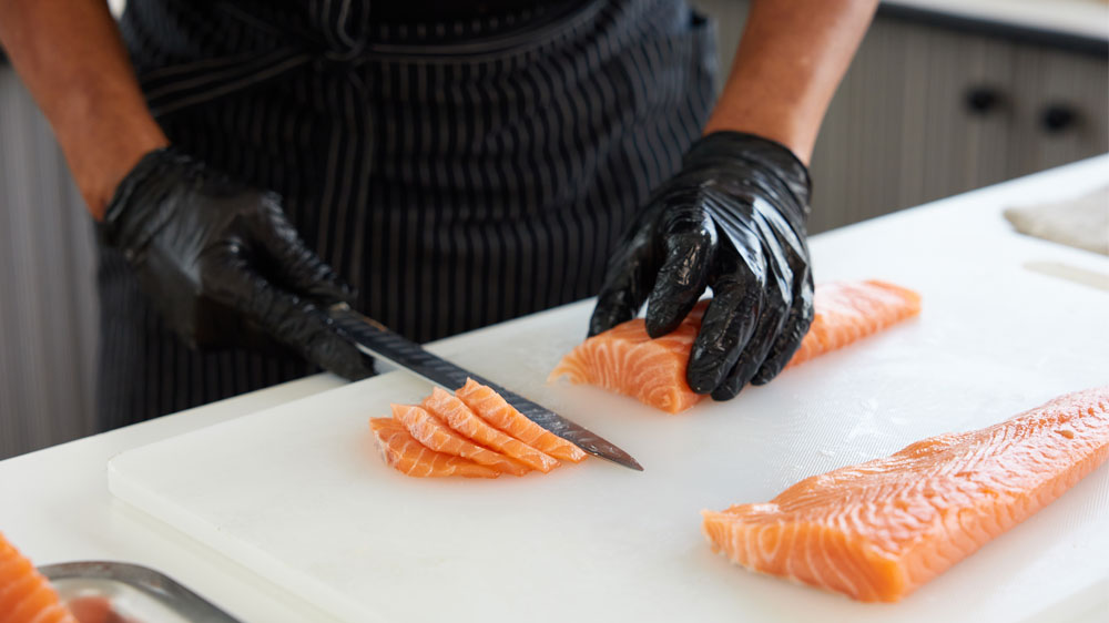 Muž v rukavicích krájí lososa na plátky dlouhým nožem_03