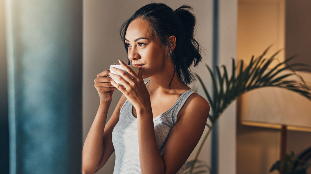 Mlad&aacute; žena vychutn&aacute;vaj&iacute;c&iacute; si &scaron;&aacute;lek k&aacute;vy ve stoje s pohledem upřen&yacute;m do d&aacute;li_05