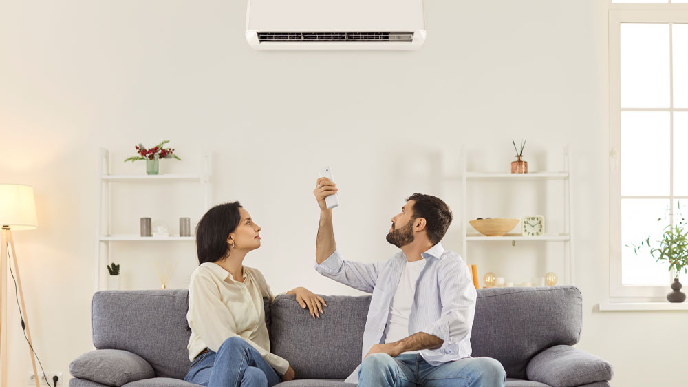 Pár sedící na pohovce a muž ovládá klimatizaci přes dálkový ovladač_03