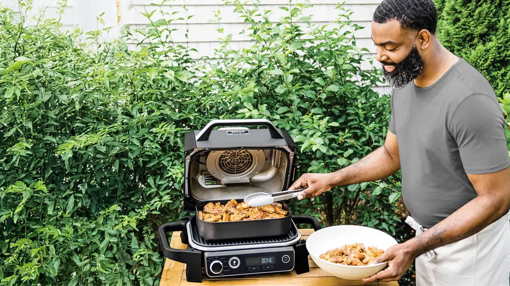 Muž u elektrického venkovního grilu Ninja OG701EU Woodfire plného masa_02