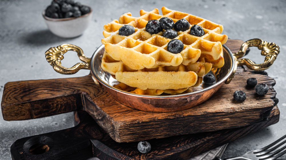 Vafle s čerstvými borůvkami ve starožitné pánvičce na dřevěném prkénku_03