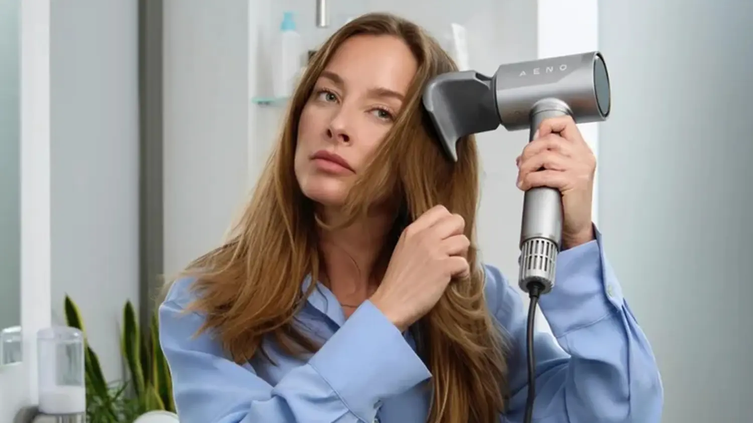 Žena foukající si vlasy fénem AENO HD5 s nasazeným nástavcem