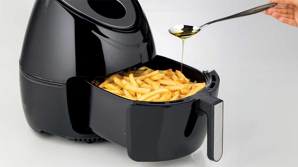 Horkovzdušná fritéza Ariete 4618 naplněná hranolkami polévanými lžičkou oleje_02