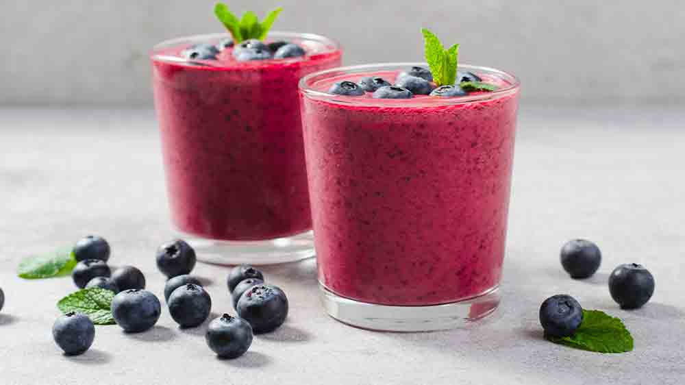 Dvě skleničky s borůvkovým smoothie a okolo čerstvé borůvky a lístky máty_04