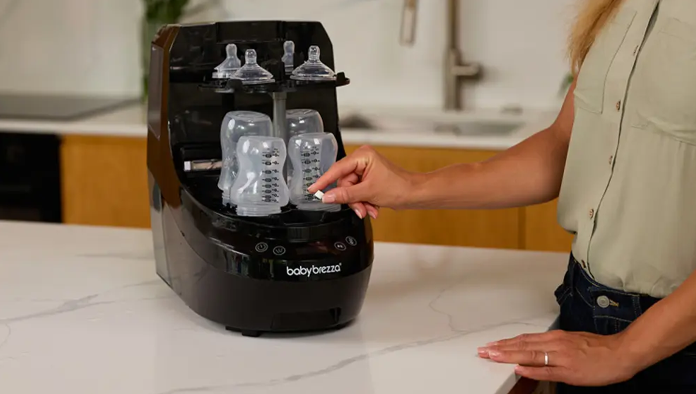 Žena u sterilizátoru Baby Brezza bottle washer pro bílo-černý lahví na kuchyňské lince