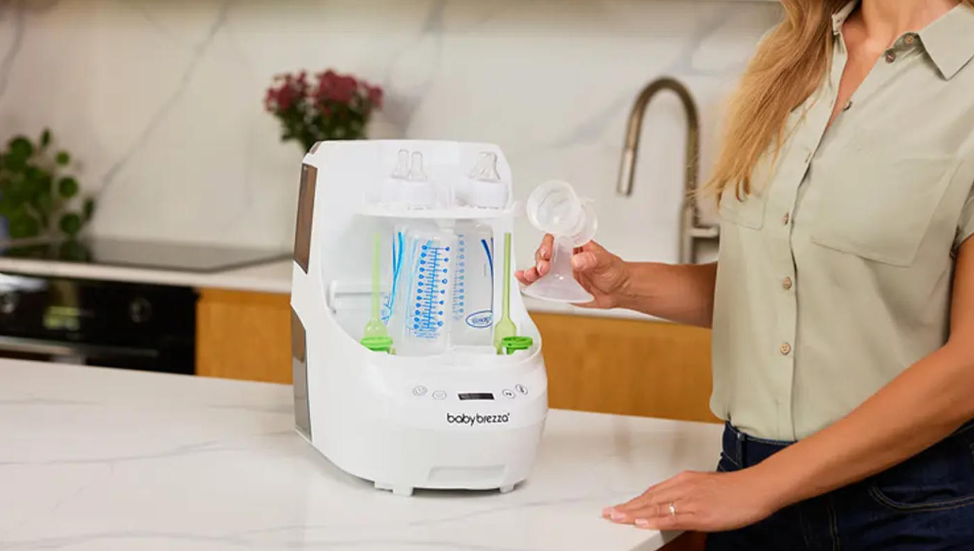 Žena u sterilizátoru Baby Brezza bottle washer pro bílo-černý lahví na kuchyňské lince