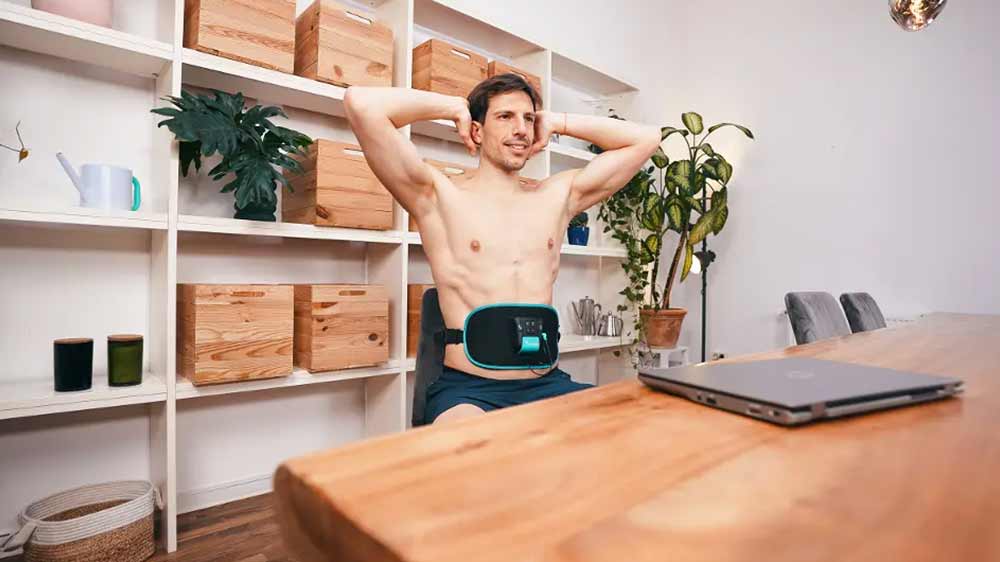 Muž sedí na židli u počítače a má nasazený elektrostimulátor Beurer Corefit I_02