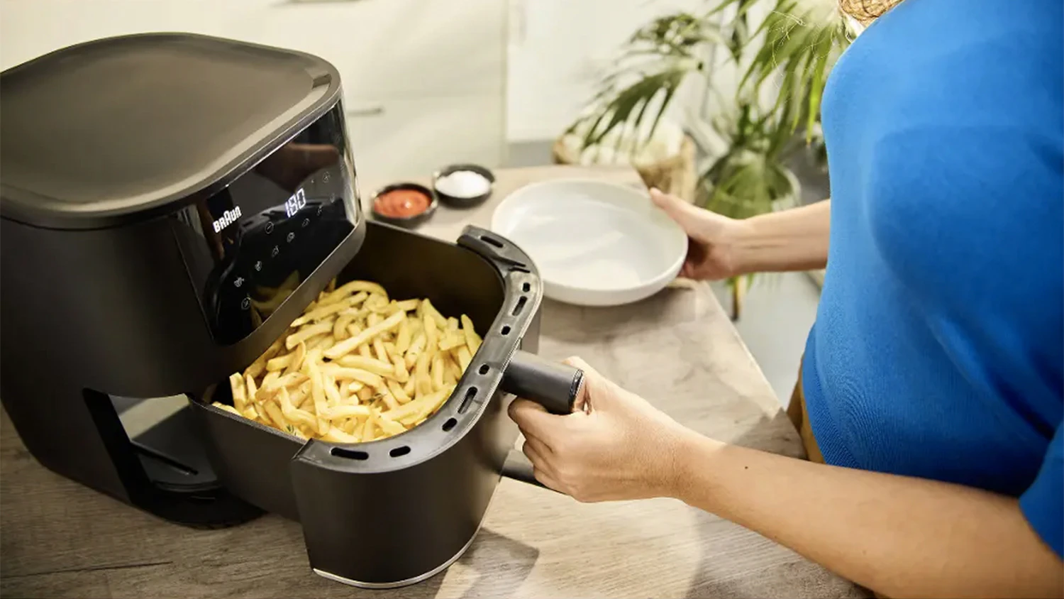 Žena vytahuje z fritézy usmažené hranolky