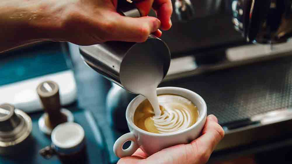 Ruka muže vytváří latte art s napěněným mlékem