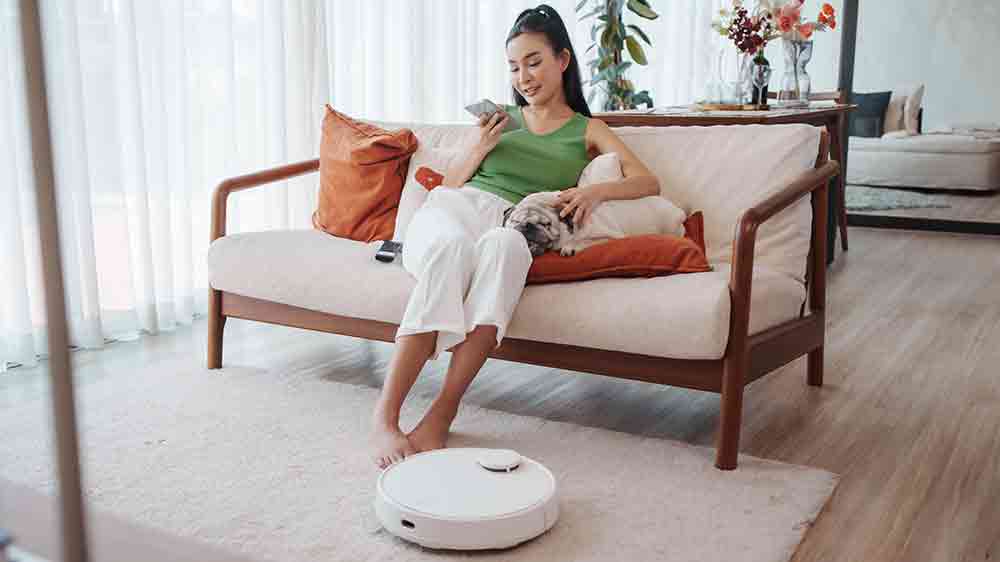 Žena sed&iacute; na pohovce a robotick&yacute; vysavač ukl&iacute;z&iacute;_02